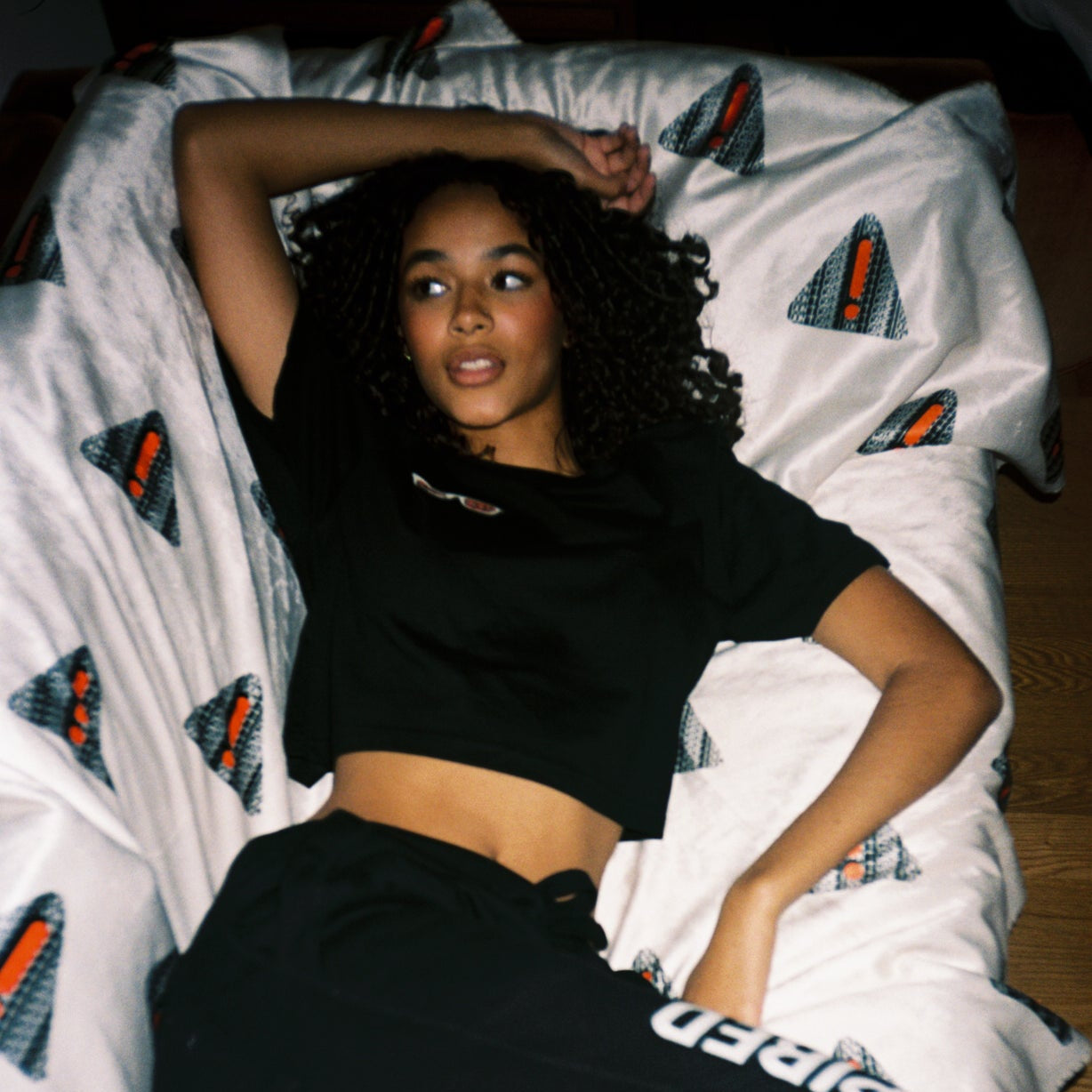 Person wearing black hoodie and pants with 'UNINSPIRED' branding, lying on a bed with patterned bedding.